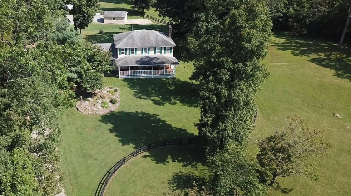 Aerial view of a wide maintained lawn, house, and curved fence line